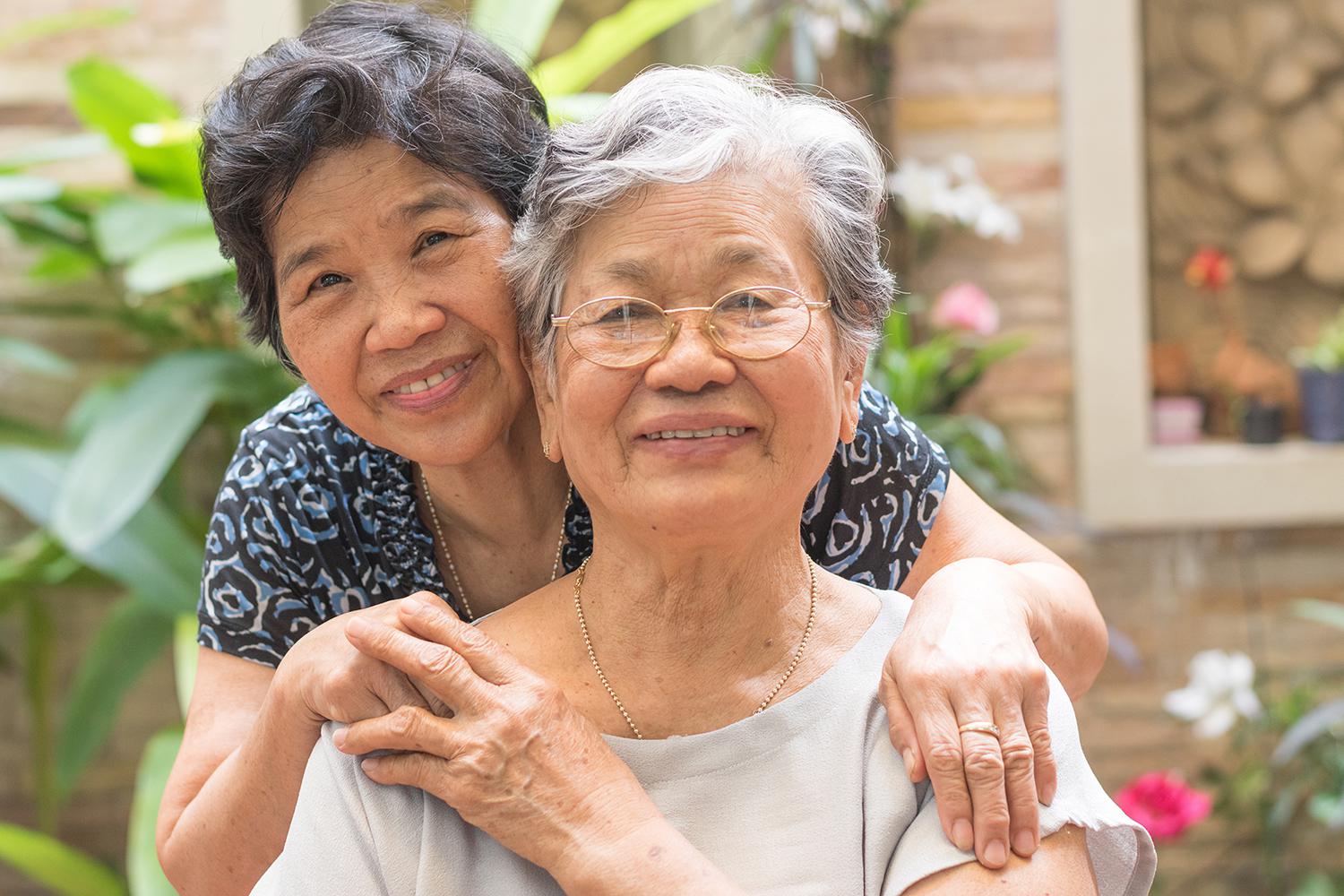 Adult Asian woman with her arms around her aging mother.