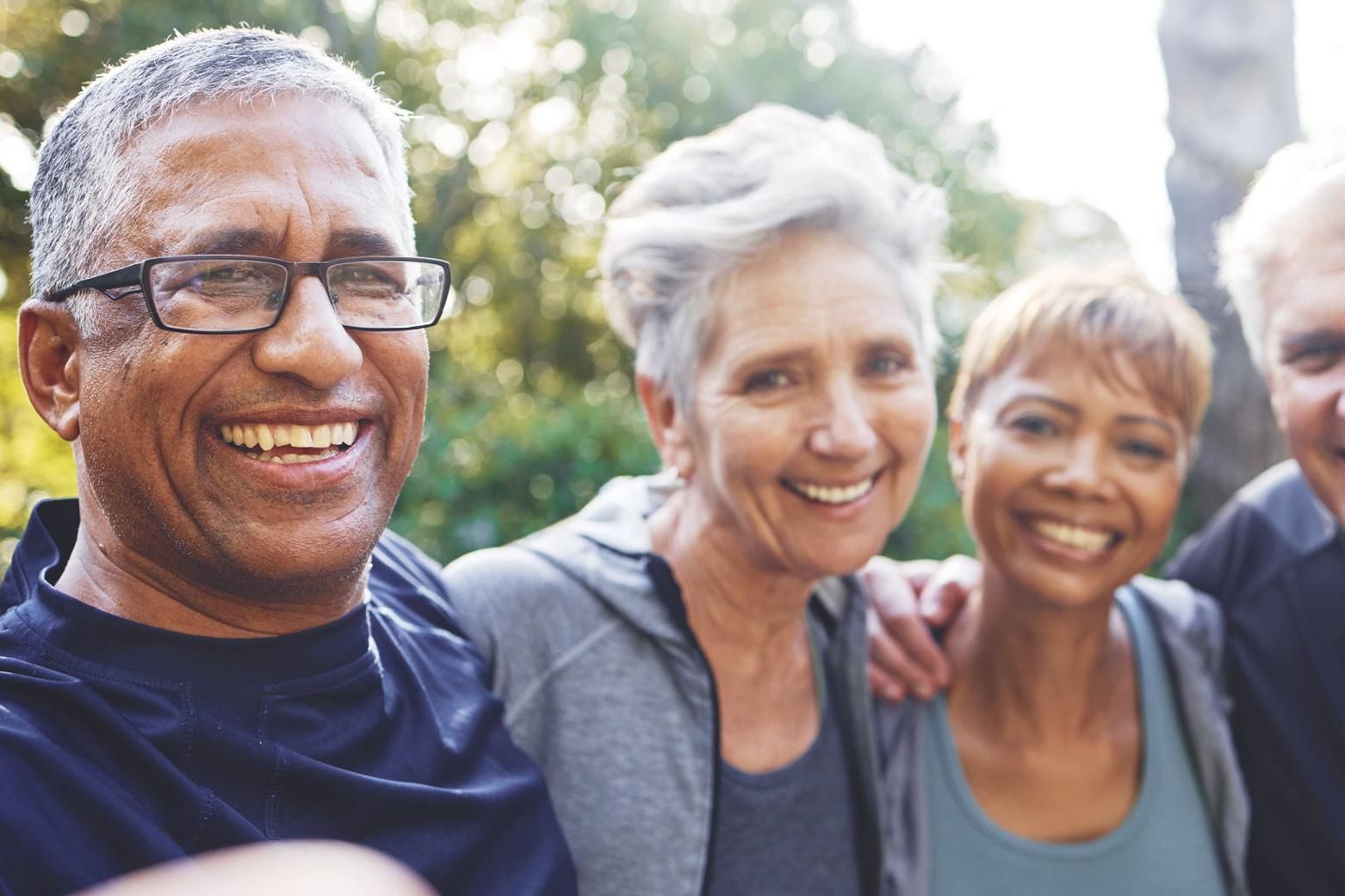 Group of diverse aging adults smiling with arms around each other's shoulders.