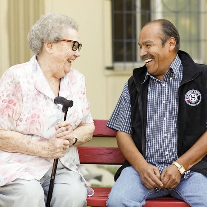 Older woman and older man sitting on a bench and smiling at each other.
