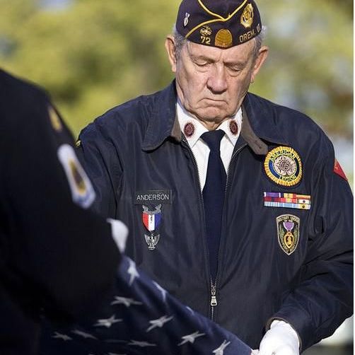 Male veteran in military uniform adorned with medal folding a U.S. flag.